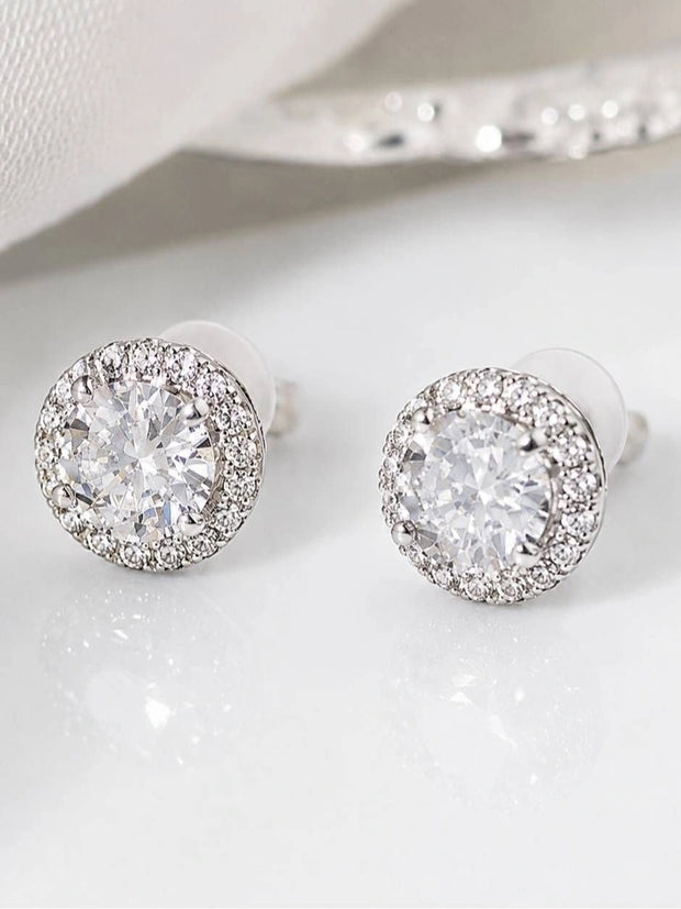 Pair of silver-finish CZ halo stud earrings with round solitaire centre and pavé surround, on white surface