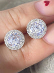 Close-up of two CZ halo stud earrings resting on a hand, showing pavé halo and large round centre stone