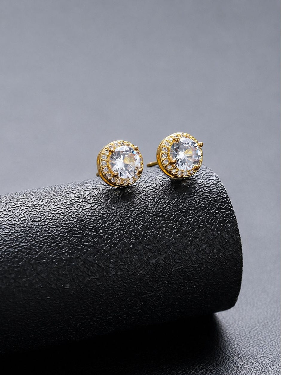 Pair of gold-plated CZ halo stud earrings resting on a curved black surface