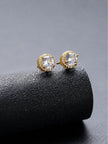 Pair of gold-plated CZ halo stud earrings resting on a curved black surface