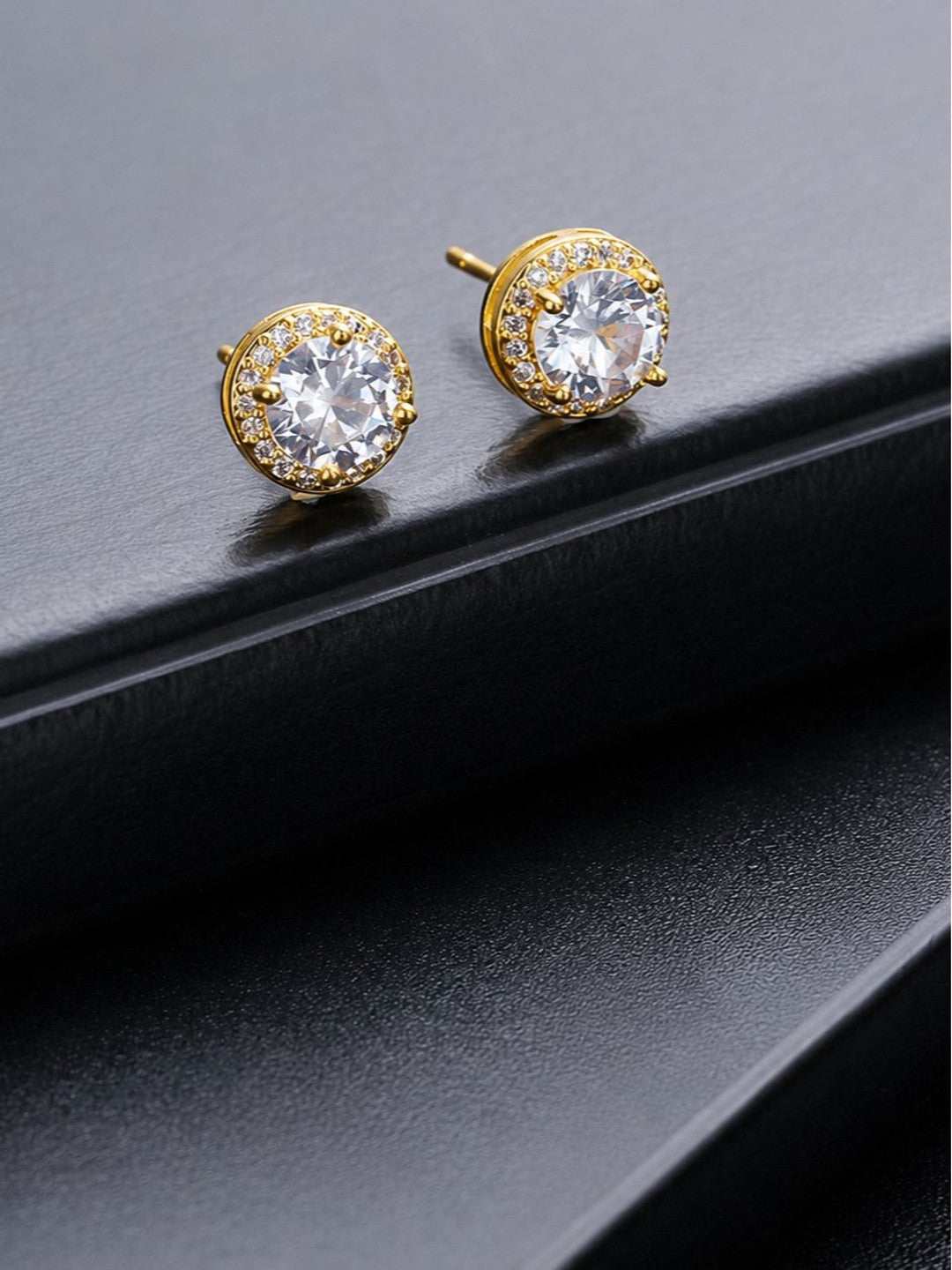 Gold-plated CZ halo stud earrings placed on edge of a dark black surface