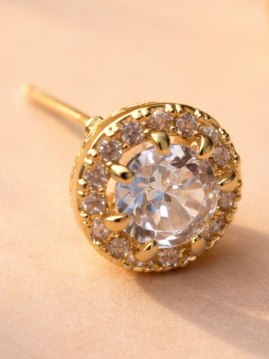 Pair of gold halo stud earrings with push-back posts lying on a cream surface