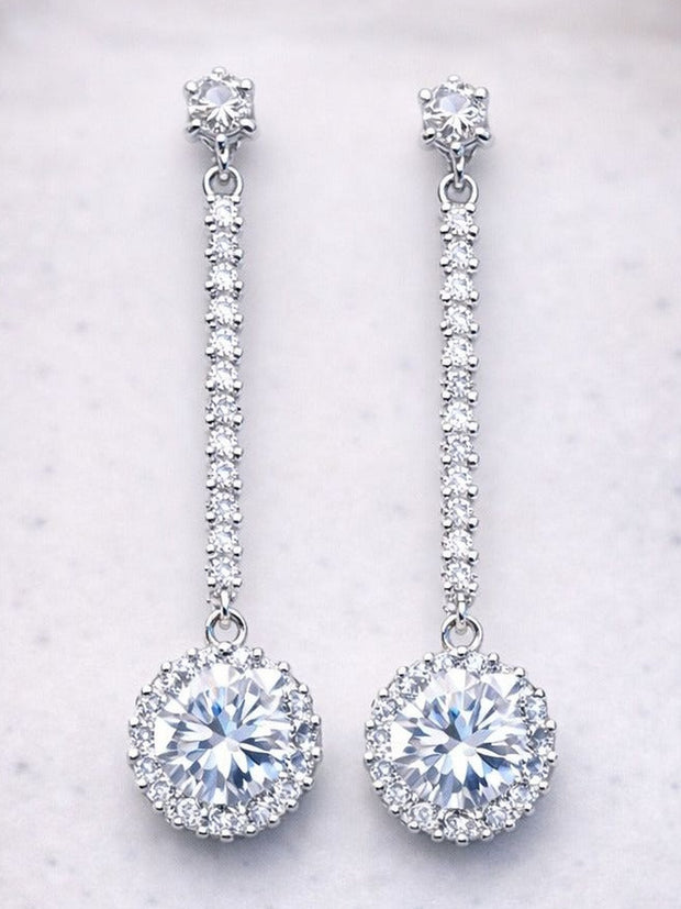 Pair of silver CZ halo drop earrings laid flat on a white marble surface showing full length