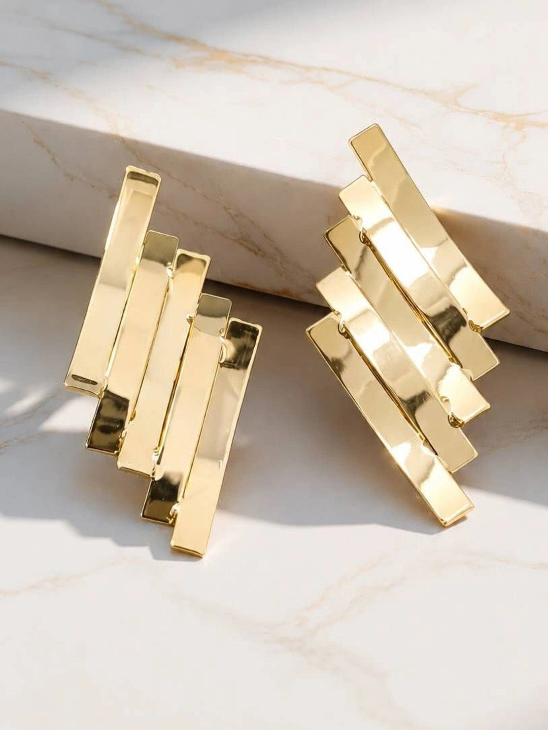 Pair of gold-toned layered rectangular bar stud earrings displayed on white marble surface