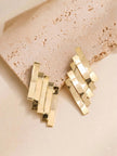 Gold geometric layered bar earrings resting on a textured beige stone surface