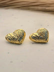Pair of gold-plated ridged heart stud earrings on a white marble surface with dried grass in background