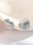 Pair of chunky silver-tone heart stud earrings with ridged molten texture on a cream surface