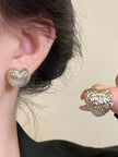 Silver textured heart stud worn on a model's ear with second earring held between fingers