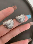 Two silver hammered heart studs resting on a model's open palm against a dark plate