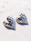 Two silver molten heart stud earrings placed side by side on a white marble surface