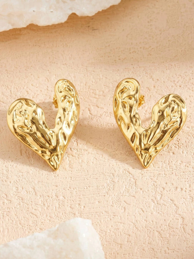 Both gold hammered heart stud earrings displayed upright on a textured pink stone surface
