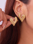 Model wearing oversized gold hammered heart stud earrings on both ears, hair tucked back