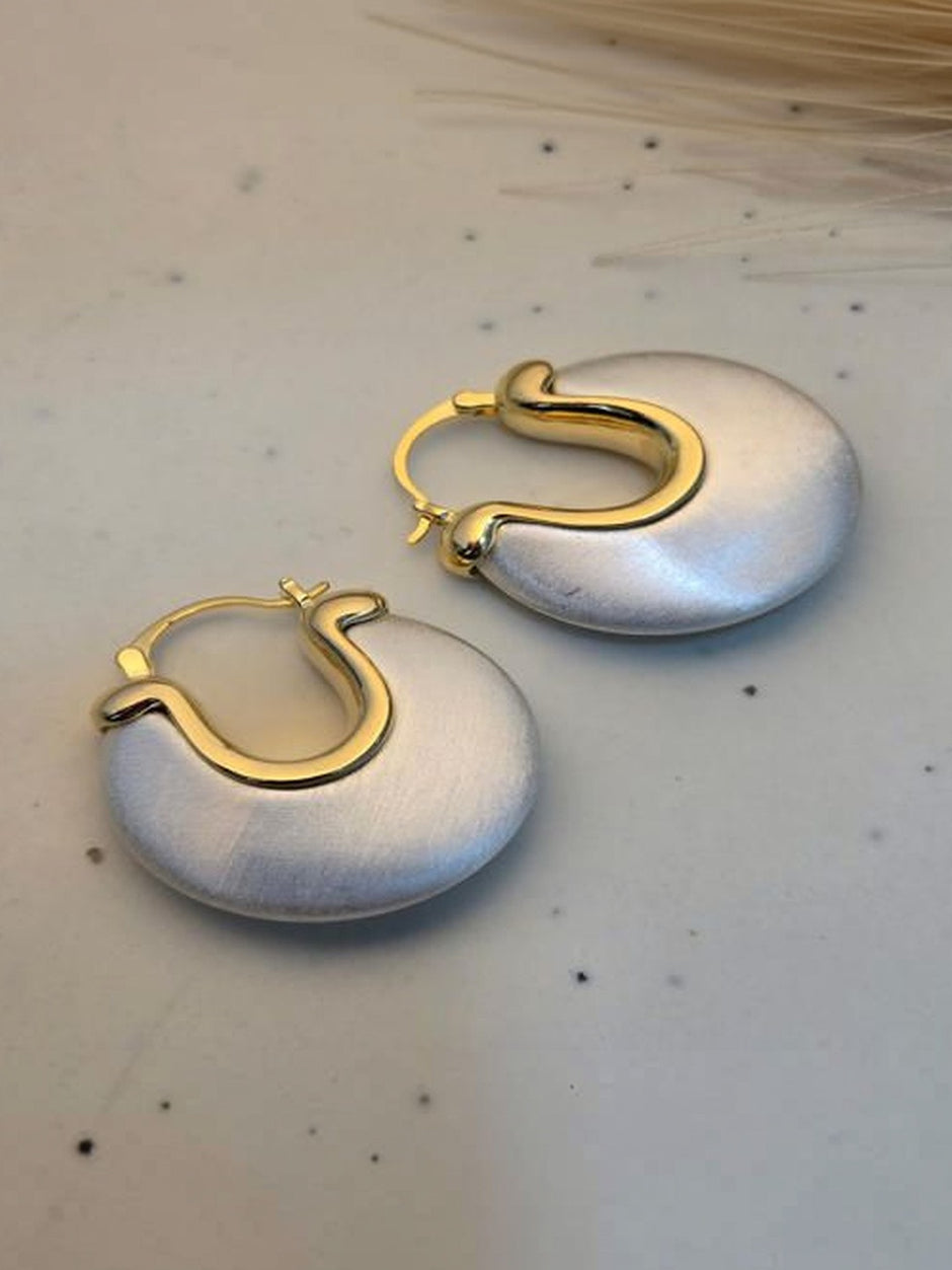 Pair of chunky crescent hoop earrings with brushed silver-finish disc and polished gold-tone lever-back clasp on a light speckled surface