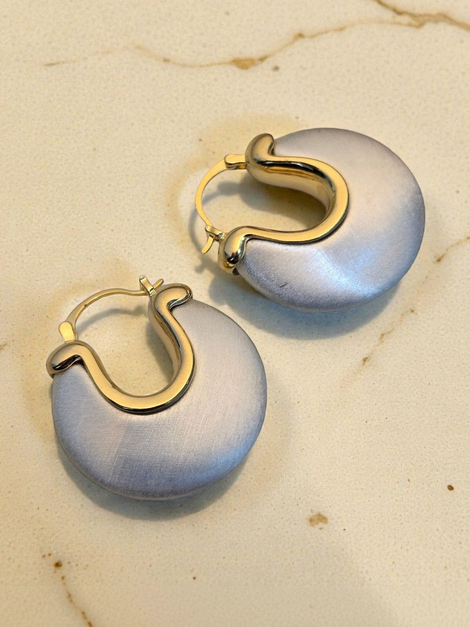 Close-up of silver and gold-tone chunky hoop earring pair resting on a warm marble surface