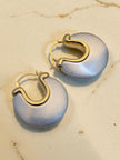Close-up of silver and gold-tone chunky hoop earring pair resting on a warm marble surface