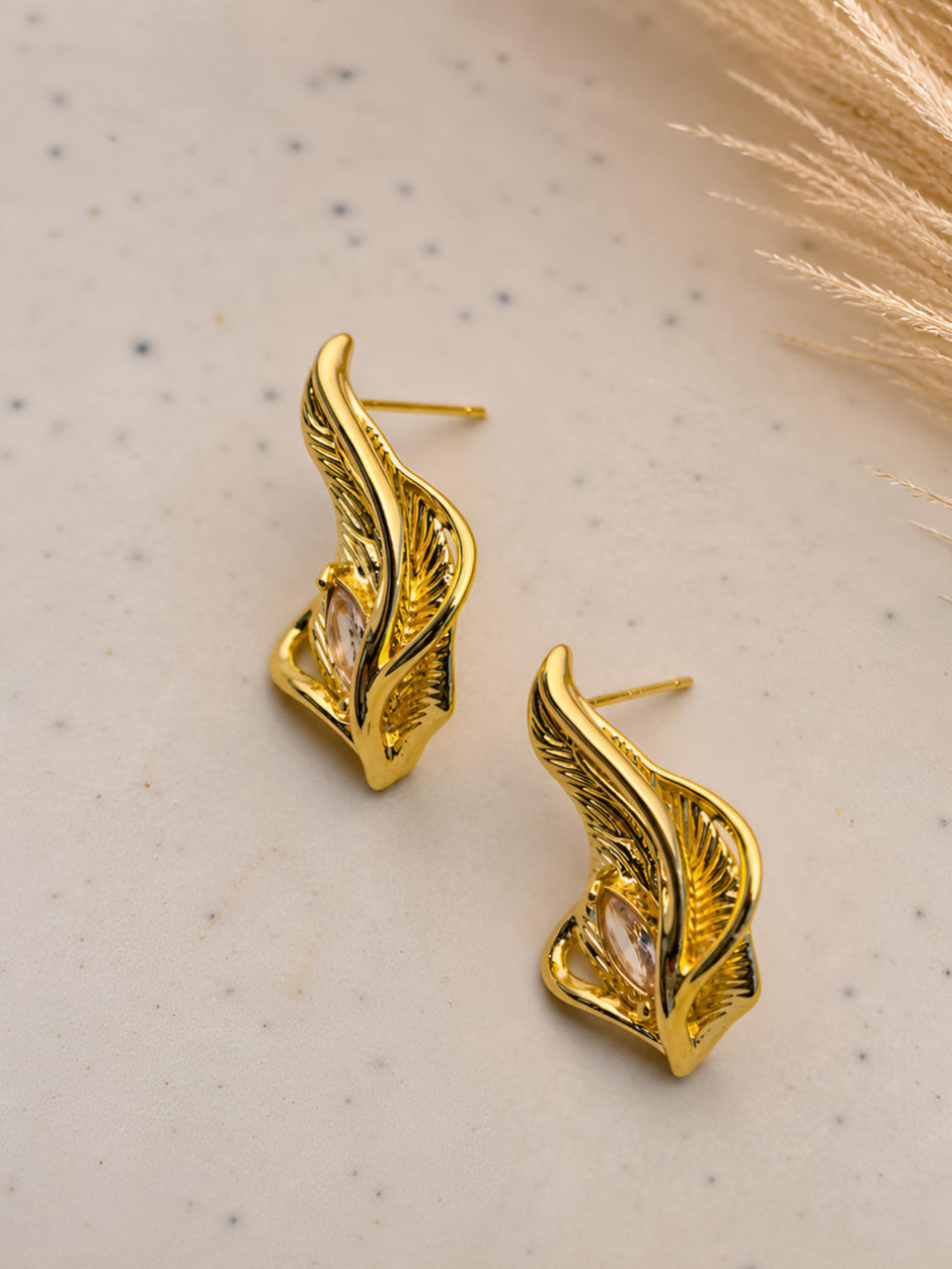 Side view of gold feather stud earrings showing push-back posts on a speckled white surface