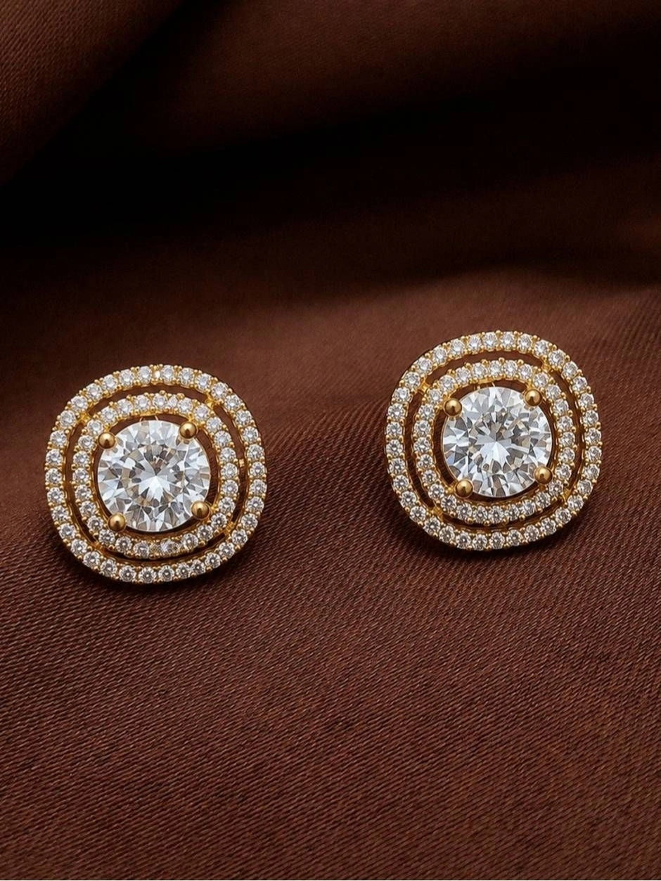 Pair of gold-plated double halo CZ stud earrings laid flat on dark brown fabric