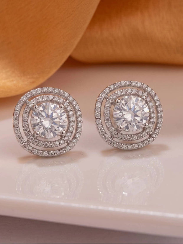 Pair of silver double halo CZ stud earrings displayed flat on a white marble surface
