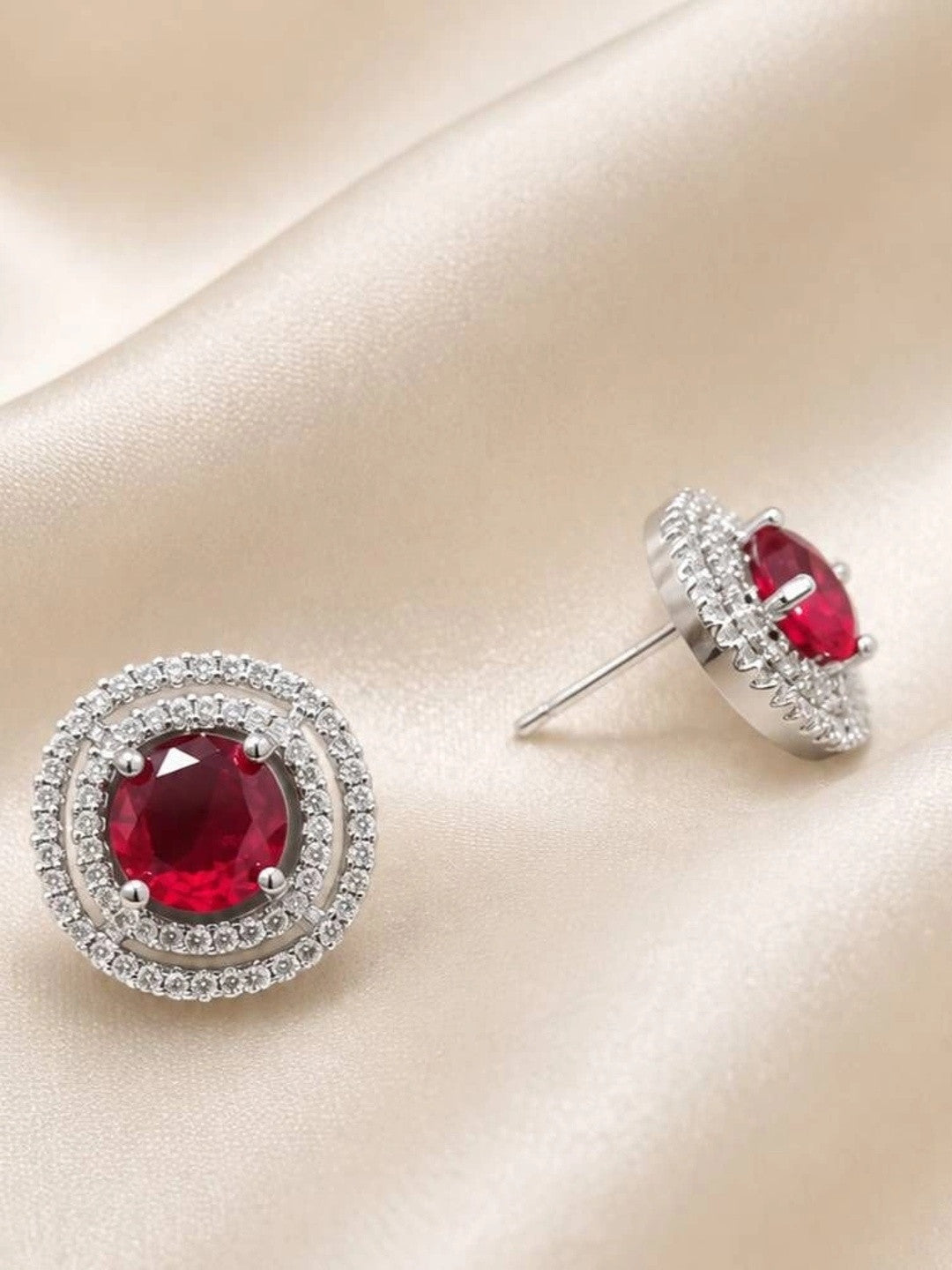 Silver double halo stud earrings with ruby red crystal centre on cream satin, one shown from front and one from side