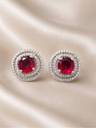 Pair of silver-tone double halo ruby red stud earrings laid flat on cream satin fabric