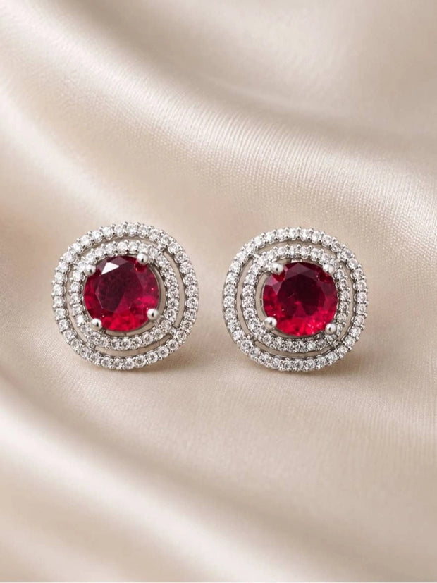 Pair of silver-tone double halo ruby red stud earrings laid flat on cream satin fabric