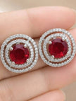 Close-up of silver double halo ruby red stud earrings held in an open palm showing scale