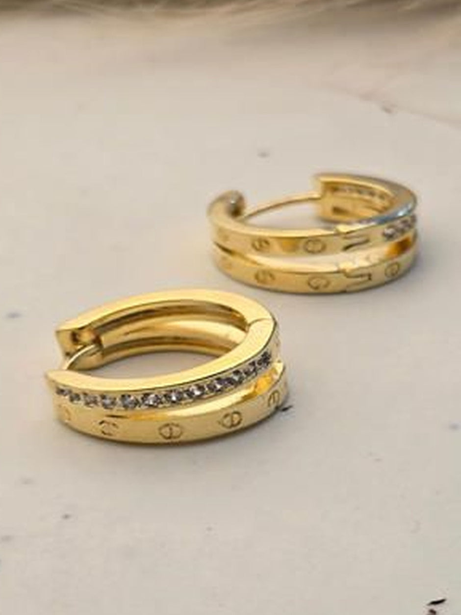 Pair of gold-plated double band huggie hoop earrings with crystal row on a marble surface
