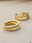 Pair of gold-plated double band huggie hoop earrings with crystal row on a marble surface