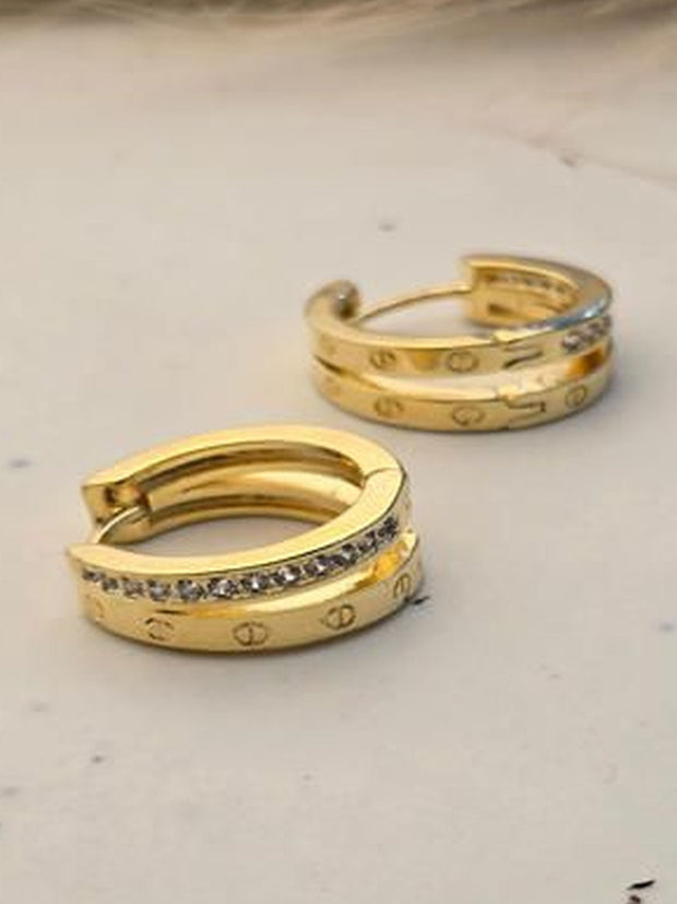 Pair of gold-plated double band huggie hoop earrings with crystal row on a marble surface