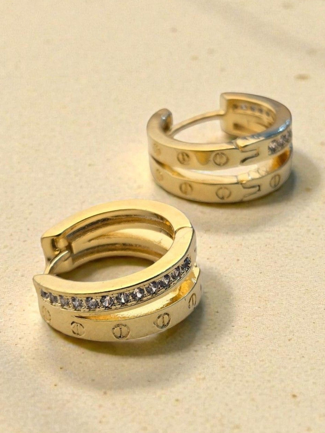 Close-up of gold double band crystal hoop earrings showing screw motif detail on sandy background
