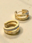 Close-up of gold double band crystal hoop earrings showing screw motif detail on sandy background