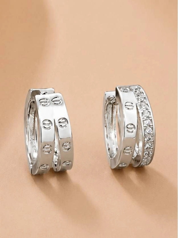 Pair of silver-tone double hoop earrings with crystal pavé band and screw-head detailing on a beige surface