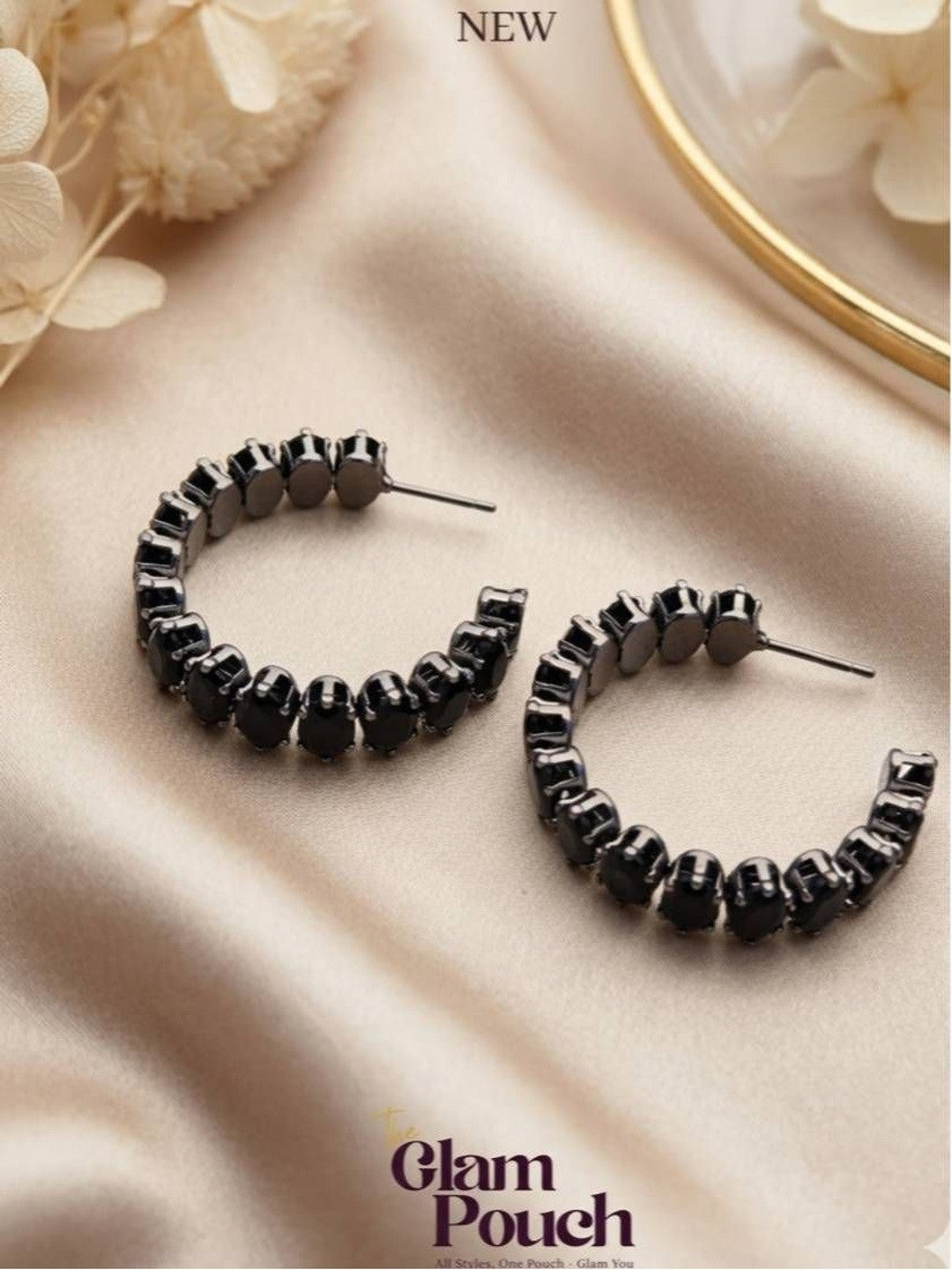 Pair of black-plated oval crystal hoop earrings laid flat on cream satin fabric