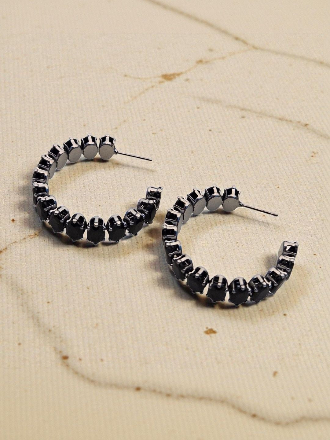 Two black crystal hoop earrings with post fastening placed on a marble surface