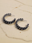 Two black crystal hoop earrings with post fastening placed on a marble surface