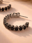 Close-up of one black-plated hoop earring showing prong-set oval stones and post back