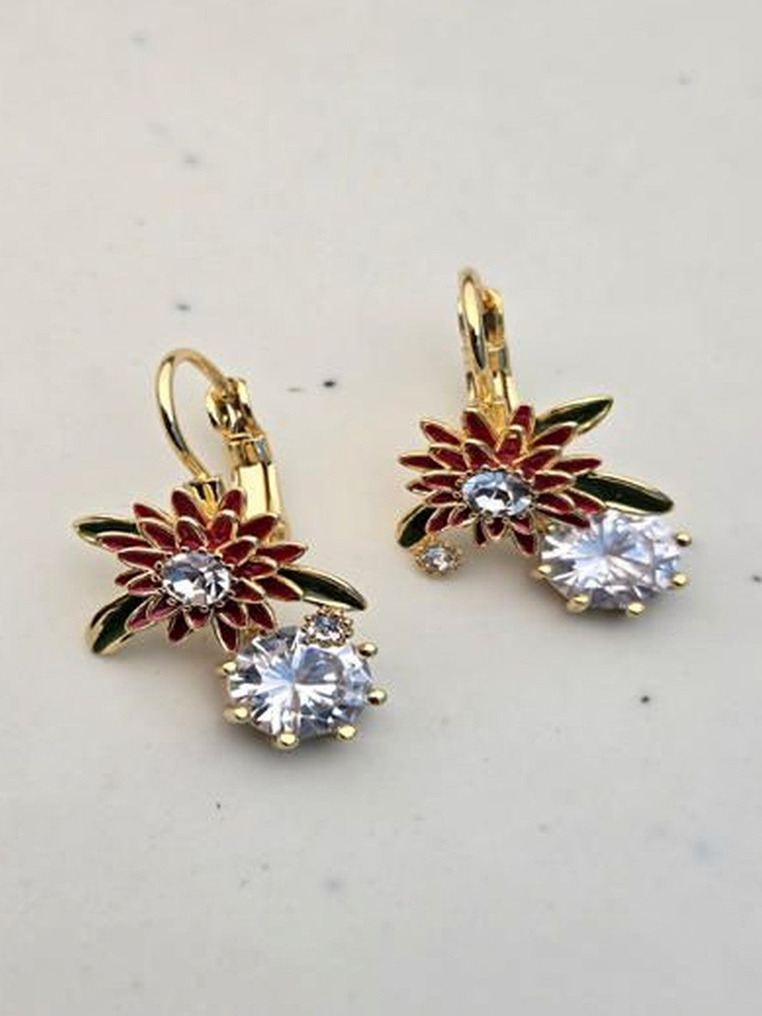 Pair of gold-plated red enamel flower drop earrings with crystal stones on marble surface