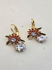 Pair of gold-plated red enamel flower drop earrings with crystal stones on marble surface