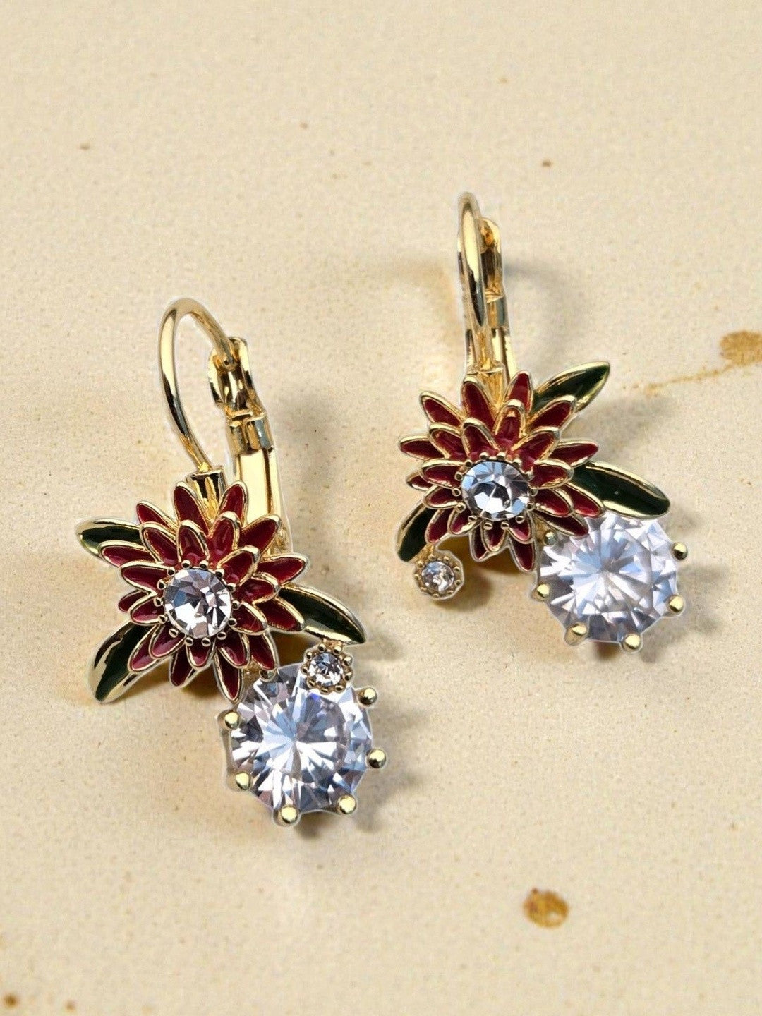 Red enamel and gold flower drop earrings with cubic zirconia stones on sandy surface