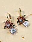 Red enamel and gold flower drop earrings with cubic zirconia stones on sandy surface