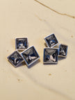Close-up of blue crystal square cluster stud earrings on a linen fabric surface showing bezel settings and stud post