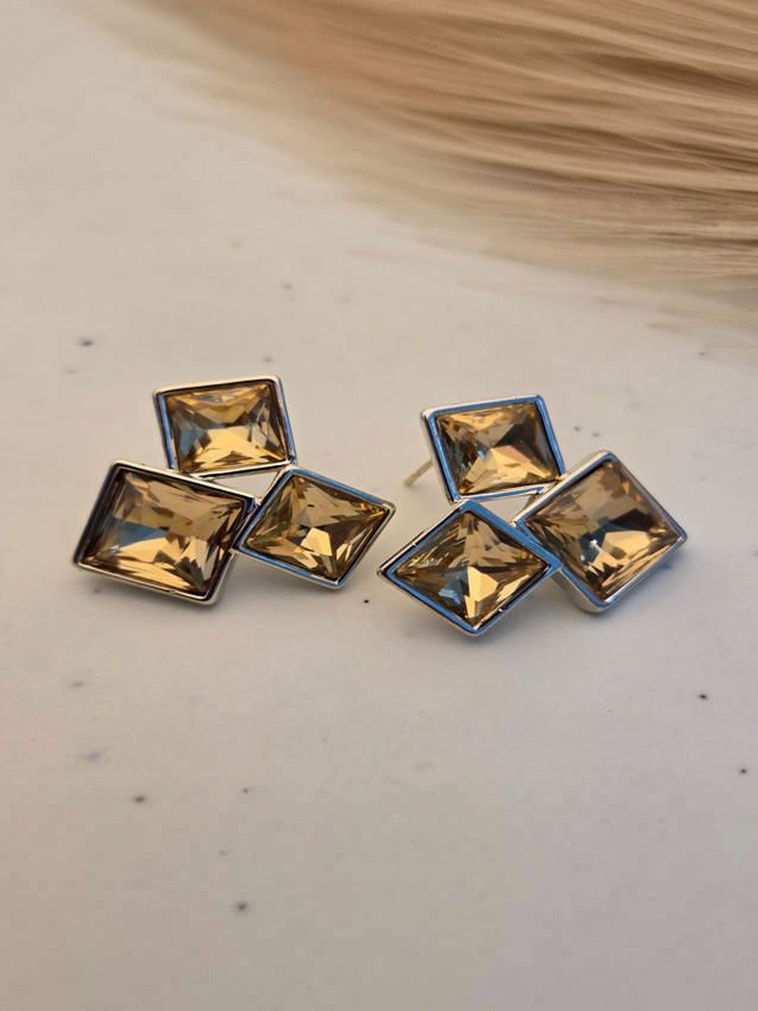 Pair of silver-finish square crystal cluster stud earrings on a white surface with neutral background
