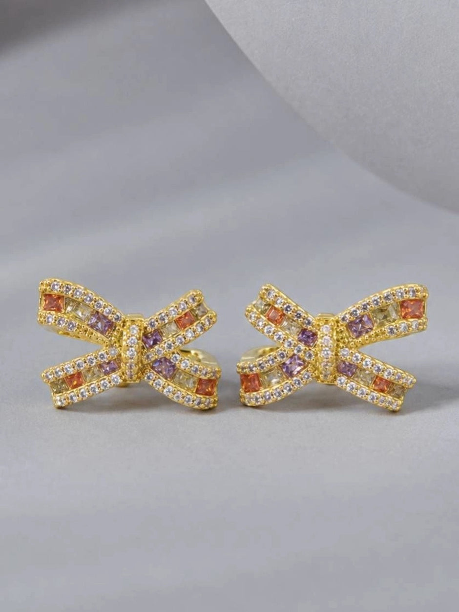 Pair of gold-plated bow stud earrings with multicolour zirconia, front view on grey surface