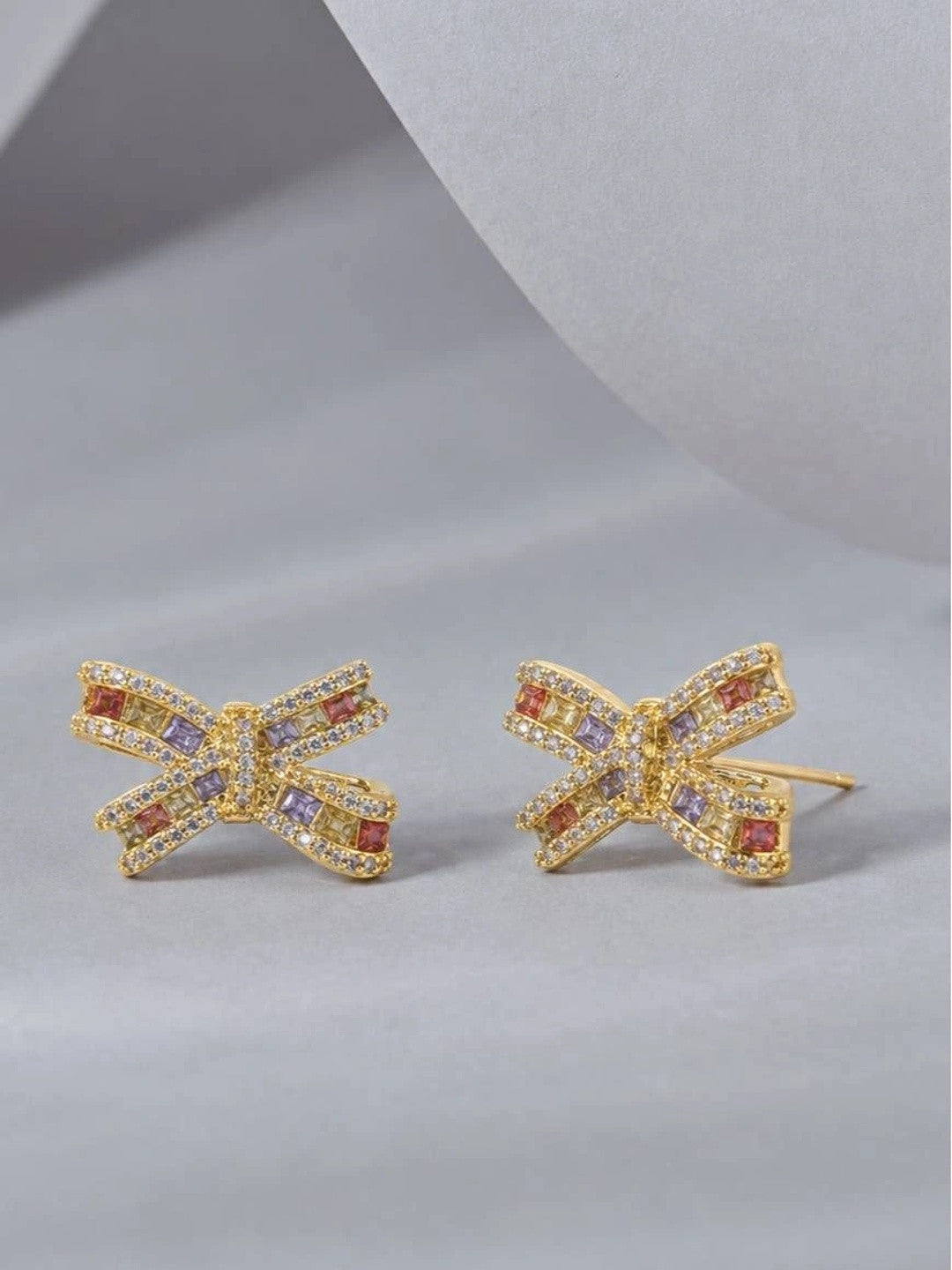 Two gold bow stud earrings with orange, lavender and yellow stones, angled flat-lay view