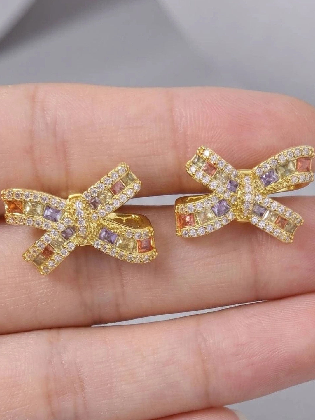 Close-up of multicolour CZ bow stud earrings held in a hand showing stone detail and size