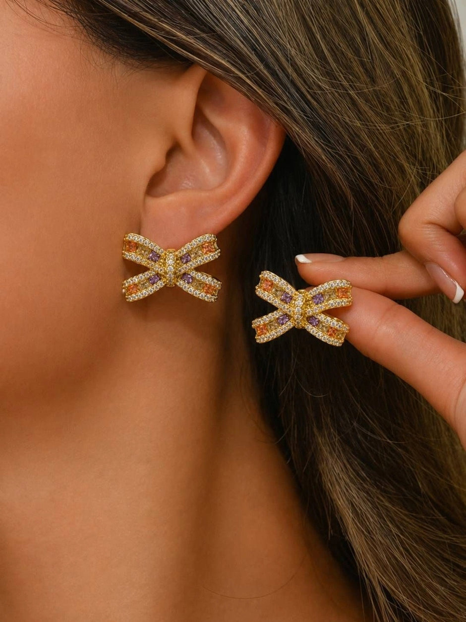 Model wearing gold bow stud earrings on ear, second earring held in fingers showing wearability