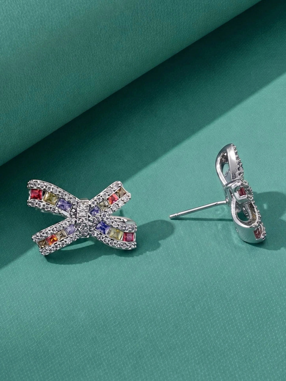 Pair of multicolour cubic zirconia bow stud earrings side by side on teal background