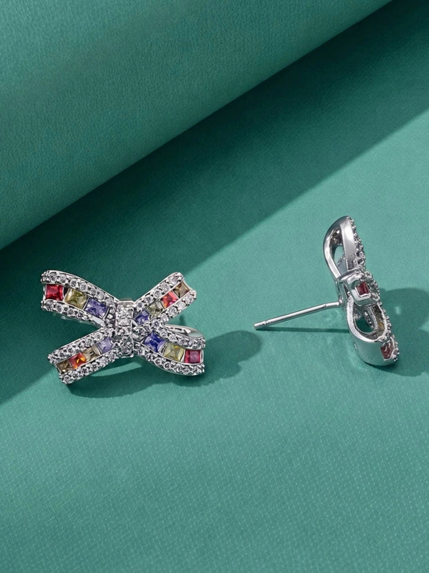 Pair of multicolour cubic zirconia bow stud earrings side by side on teal background
