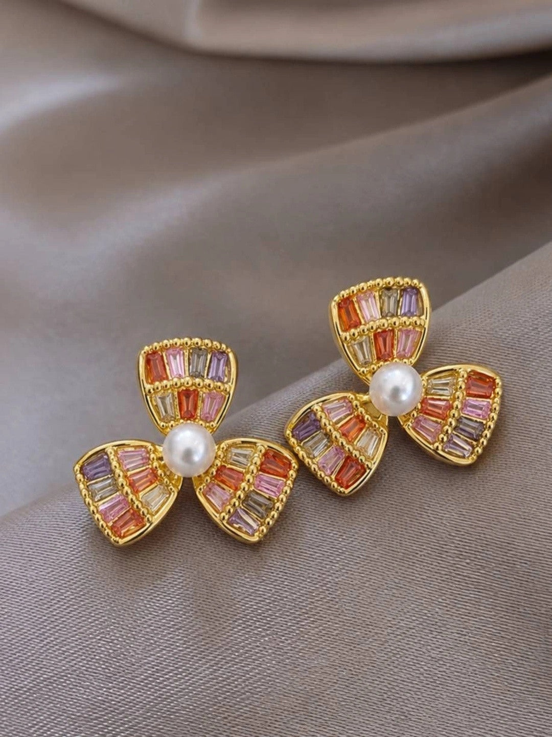Pair of gold-plated three-petal flower stud earrings with multicolour baguette zirconia stones and faux pearl centres on grey satin
