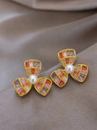Pair of gold-plated three-petal flower stud earrings with multicolour baguette zirconia stones and faux pearl centres on grey satin